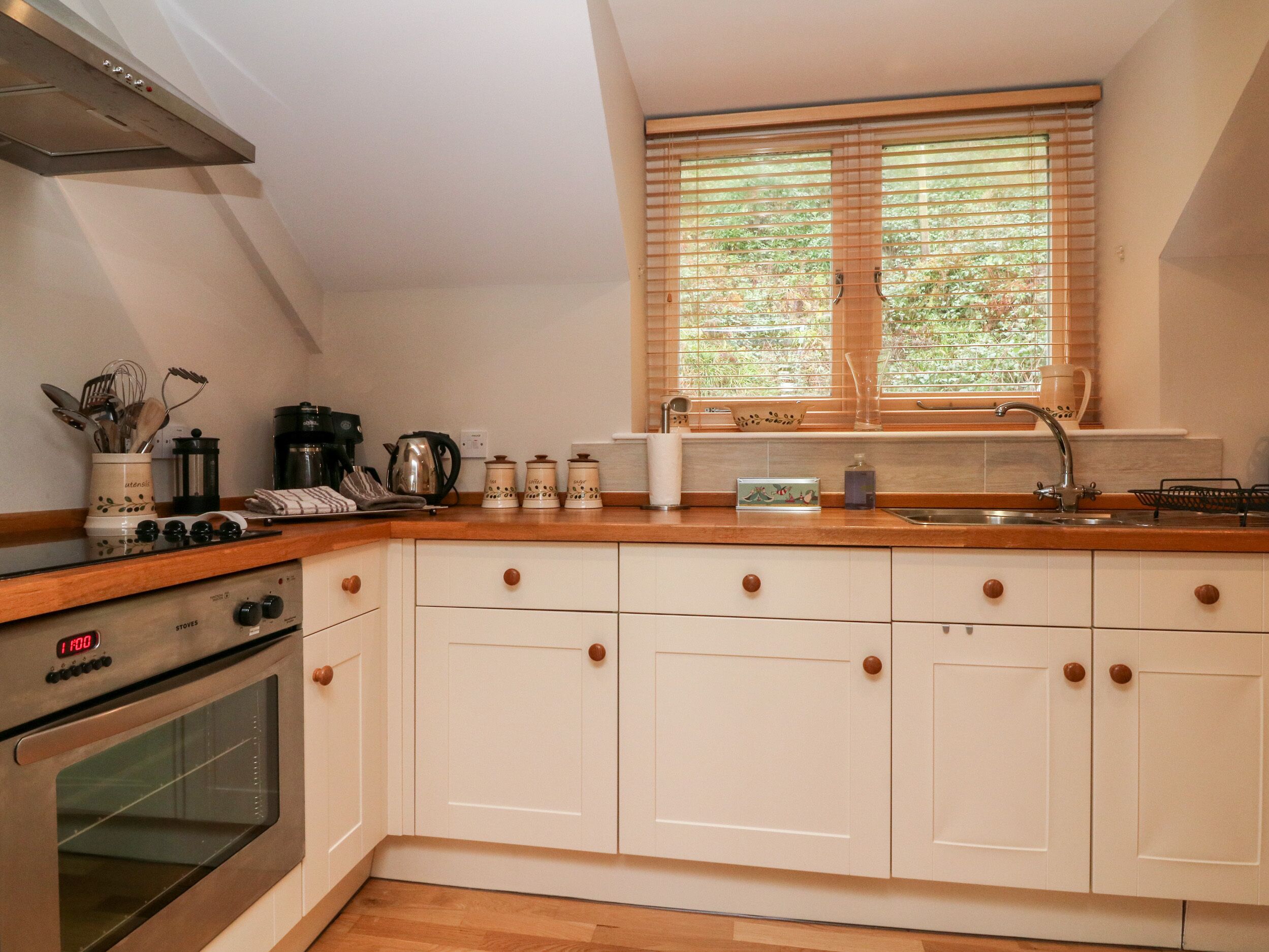 A kitchen with white cabinets, a wooden countertop, a stove, a window with blinds, and a sink.
