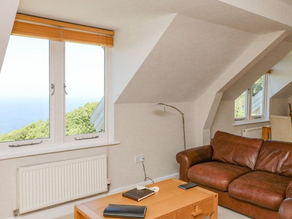 A cozy living room with a brown leather sofa, a wooden coffee table, and a view of the sea through large windows.