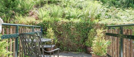 A patio with metal chairs and a table, surrounded by lush greenery and a wooden fence.