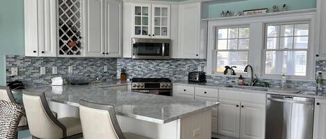 A modern kitchen with white cabinetry, a large island with bar stools, a microwave, stove, and dishwasher.