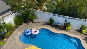 Une piscine avec deux bouées gonflables, un parasol jaune et une clôture blanche.