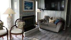 A living room with a fireplace, a sofa, two armchairs, and a television mounted on the wall.