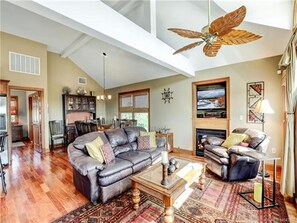 A spacious living room with a high ceiling, a fireplace, and a large window.