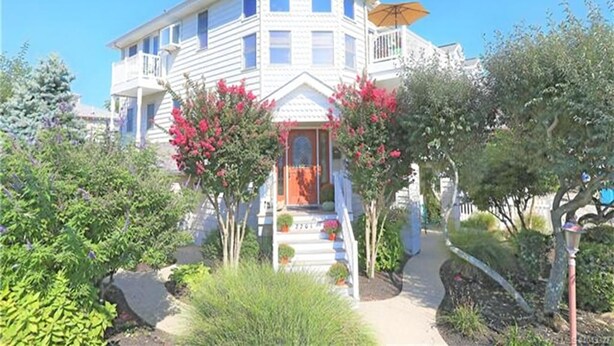 Ein zweistöckiges Haus mit Balkon, einer Veranda mit Treppe und einem Garten mit verschiedenen Pflanzen und Blumen.