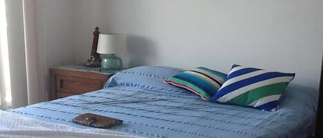 A bed with a blue and white striped bedspread, two pillows with stripes, a bedside lamp, and a small table with a lamp.