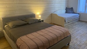 A bedroom with a large bed, a smaller bed, a nightstand with a lamp, and a wooden wall with a 'LOVE' sign.