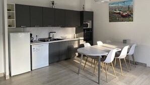 A modern kitchen with dark cabinets, a white refrigerator, and a dining area with a white table and chairs.
