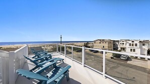 Un balcon avec des chaises bleues, d’où l’on peut admirer la plage et les bâtiments.