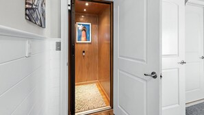 Un couloir avec une porte en bois donnant sur une pièce, un tableau encadré accroché au mur et un tapis à motifs sur le sol.
