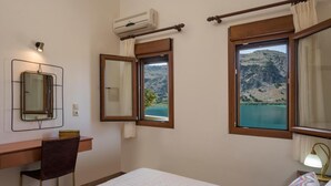 Een slaapkamer met een bed, een bureau en twee ramen met uitzicht op een bergachtig landschap.