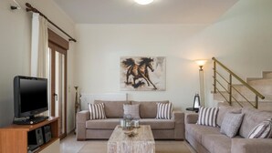 Een woonkamer met een televisie, twee banken, een salontafel, een schilderij en een trap.