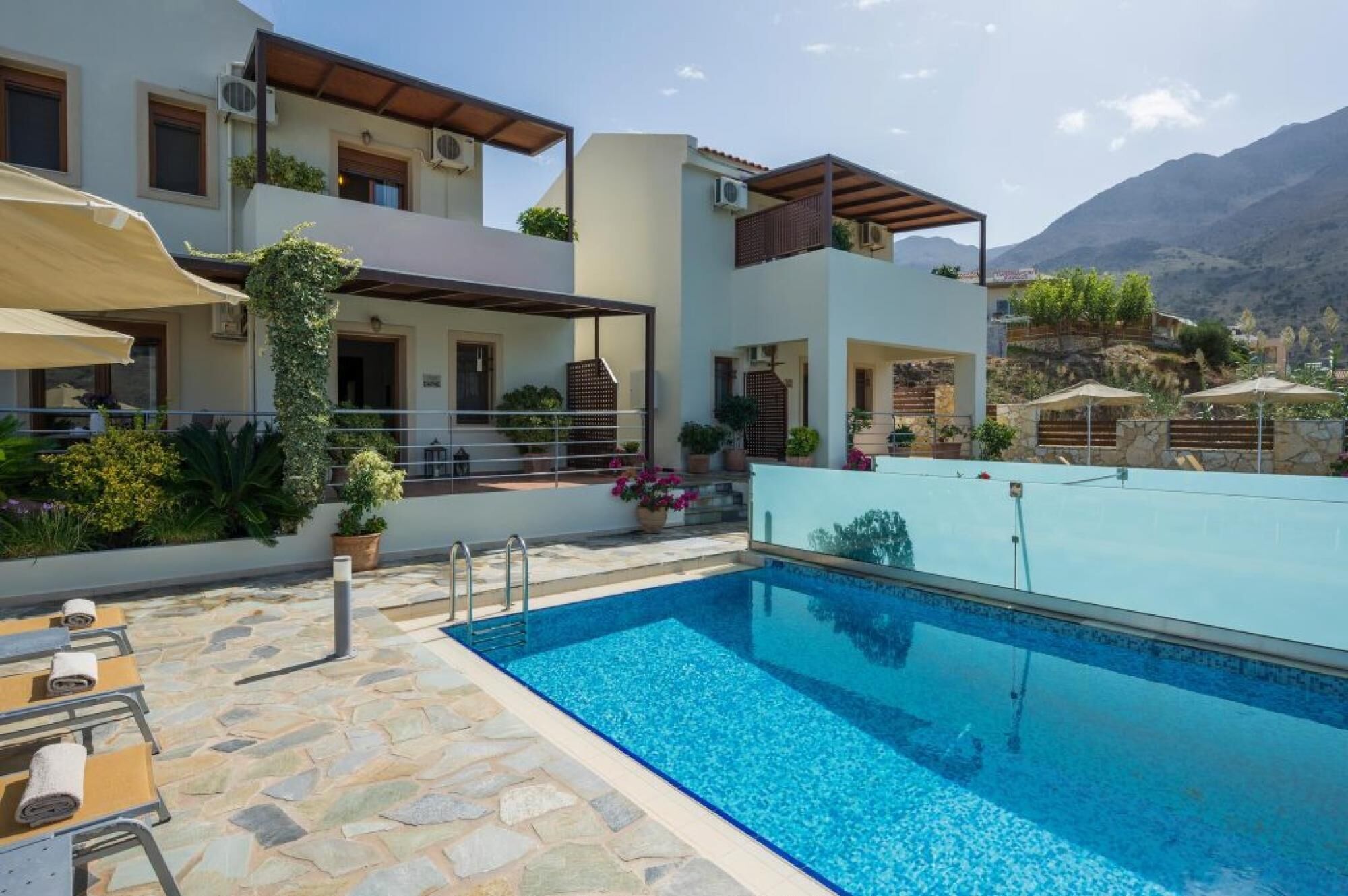 A modern villa with a swimming pool, stone flooring, and outdoor seating.