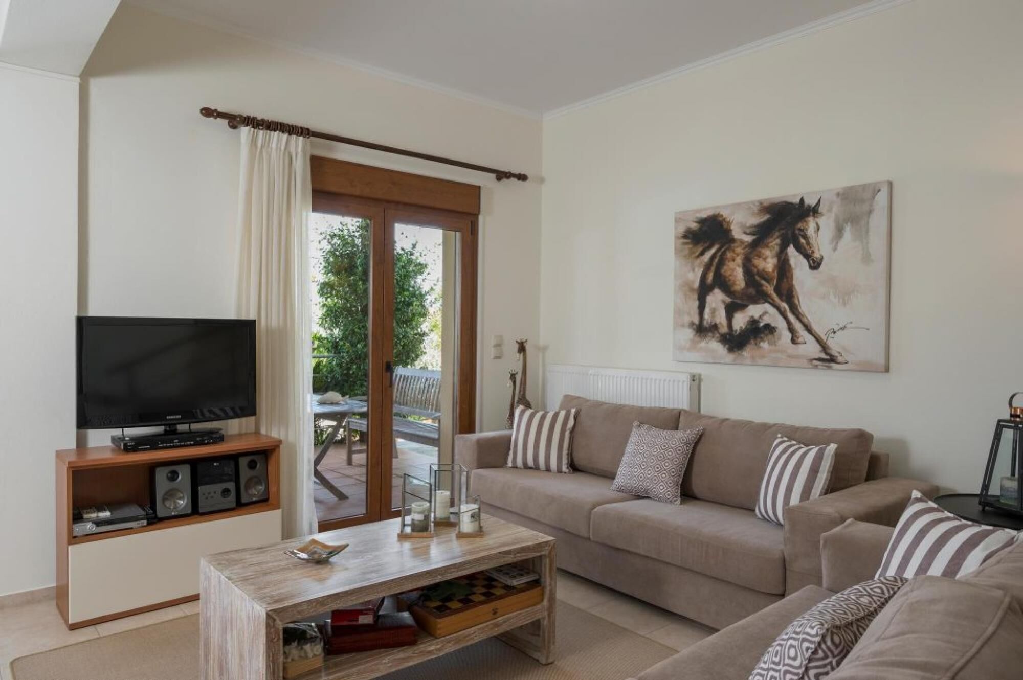 Uma sala de estar com televisão, mesa de centro, sofá e um quadro de um cavalo.