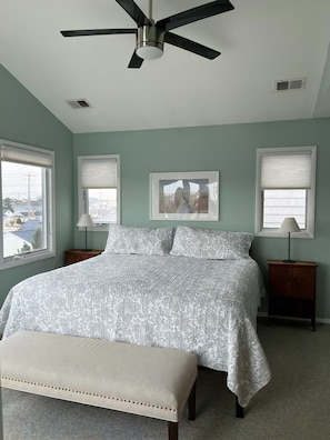 A bedroom with a bed, a bench, a ceiling fan, and two bedside tables with lamps.
