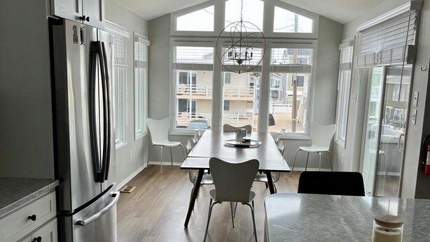 A modern kitchen with a large island, a dining area with a view, and a refrigerator.