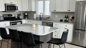 A modern kitchen with white cabinets, stainless steel appliances, a central island with bar stools, and a wooden floor.