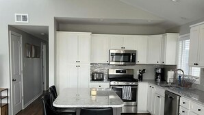 A modern kitchen with white cabinets, stainless steel appliances, a central island with bar stools, and a wooden floor.