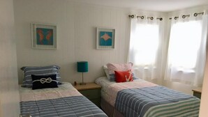 Ein Zimmer mit zwei Betten, jeweils mit gestreifter Bettwäsche, einem Nachttisch mit Lampe und zwei gerahmten Bildern an der Wand.