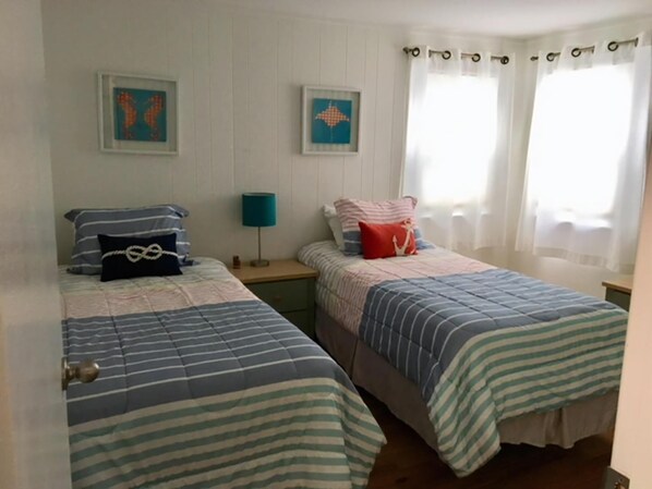 A room with two beds, each with striped bedding, a nightstand with a lamp, and two framed pictures on the wall.