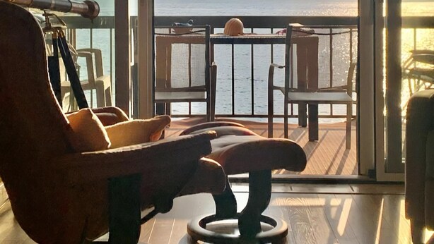 Una stanza con vista sul mare, accessibile tramite ampie porte in vetro, dotata di un pontile in legno con sedie e un'amaca.