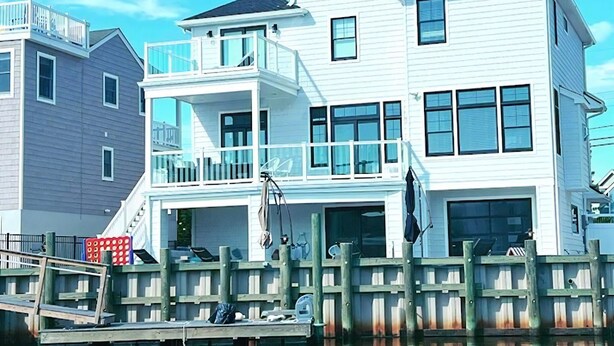 A waterfront property with a multi-story building, a dock, and a wooden fence. - BEAUTIFUL LAGOON FRONT 5 BEDROOM HOME (High Bar Harbor)