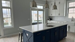 A modern kitchen with a large island, white cabinets, and pendant lighting. - BEAUTIFUL LAGOON FRONT 5 BEDROOM HOME (High Bar Harbor)