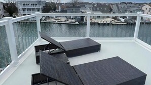 A deck with two black loungers and a glass table, overlooking a marina with boats and houses. - BEAUTIFUL LAGOON FRONT 5 BEDROOM HOME (High Bar Harbor)