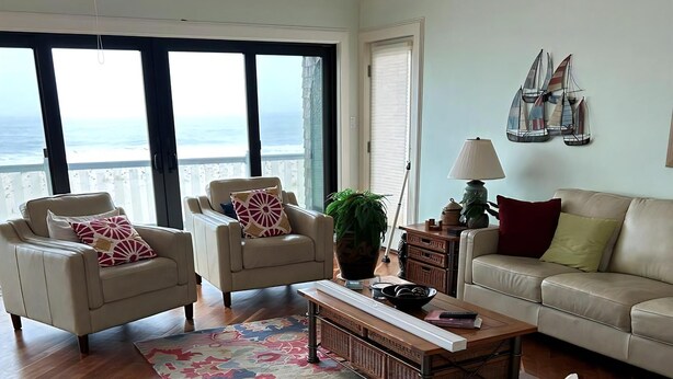 A spacious living room with a large window overlooking the ocean, a sofa, two armchairs, a coffee table, and a decorative plant. - Beautiful Private Ocean Front Home (Loveladies)