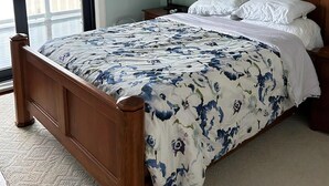 A bedroom with a bed, a ceiling fan, a window with a view, a lamp, and a wall decoration. - Beautiful Private Ocean Front Home (Loveladies)
