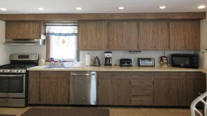 A modern kitchen with wooden cabinets, stainless steel appliances, and a window with a curtain. - Stunning home in Ship Bottom with 4 Bedrooms and Internet (Ship Bottom)