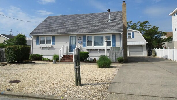 A two-story house with a front porch, a chimney, and a garage. - Stunning home in Ship Bottom with 4 Bedrooms and Internet (Ship Bottom)