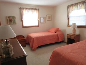 A bedroom with two beds, a nightstand with a lamp, a small table with a lamp, and a window with curtains.