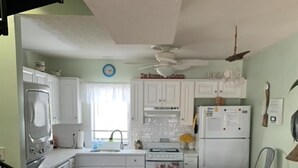 Une cuisine avec des meubles blancs, un réfrigérateur, une cuisinière et un coin repas équipé de deux chaises.