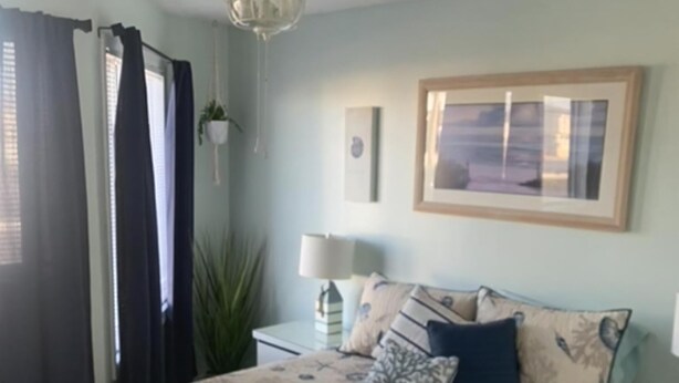 Une chambre à coucher comprenant un lit, des tables de chevet, un ventilateur de plafond, une fenêtre avec des rideaux et un tableau encadré accroché au mur.
