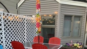 Une terrasse extérieure avec une table et des chaises, un tapis coloré et un parasol décoratif.