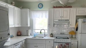 Une cuisine avec des armoires blanches, un évier, une cuisinière et un ventilateur de plafond.