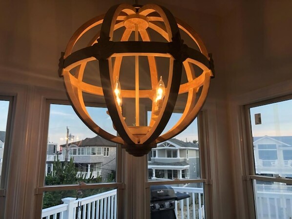 A spherical chandelier with multiple bulbs, hanging in front of a window with a view of residential buildings.