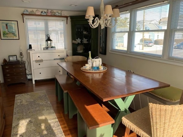 A dining area with a wooden table, benches, a chandelier, and a view of the outside.