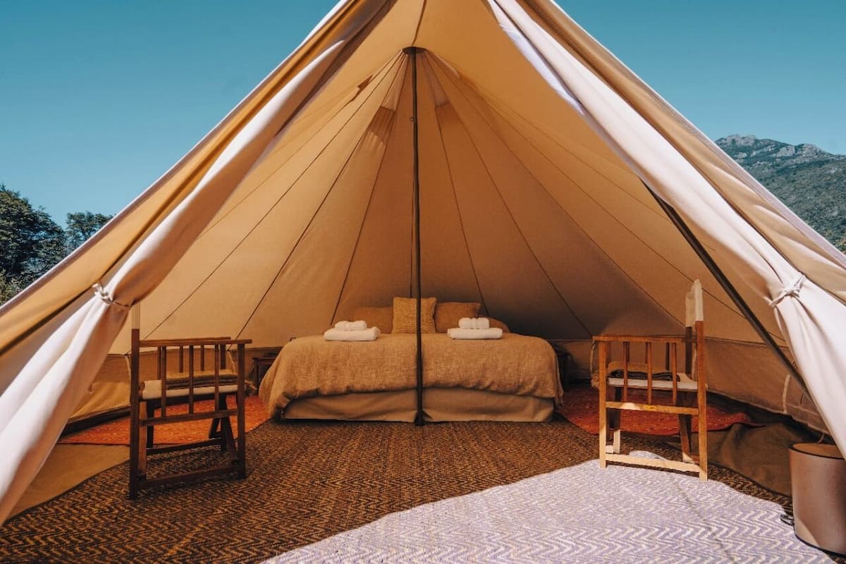 A tent with a bed, two chairs, and a small table.