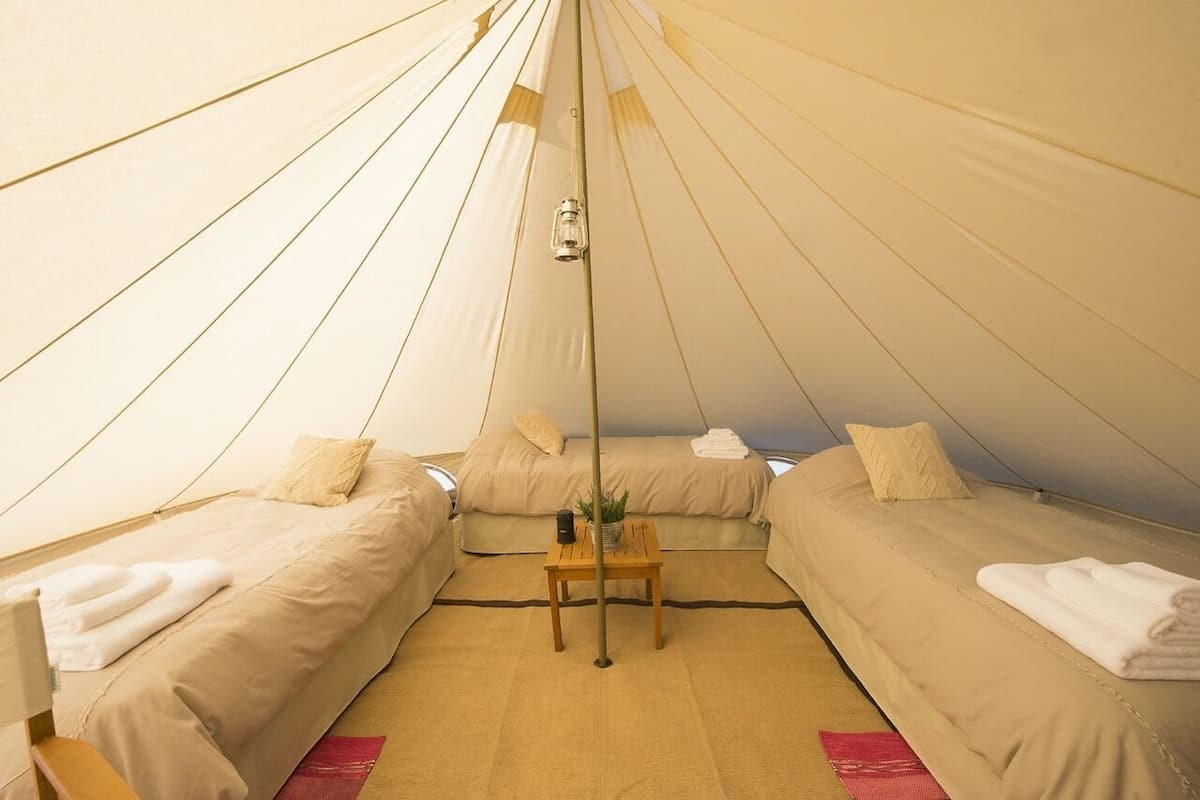 A tent-style room with two beds, a small table, and a hanging light fixture.