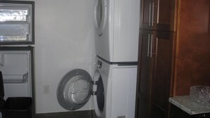 Een praktische wasruimte met een wasmachine en droger boven elkaar, een kleine prullenbak en een aanrecht met een glazen schaal.