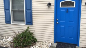 Een huis met een blauwe deur, een raam met blauwe luiken en een plantje ervoor.