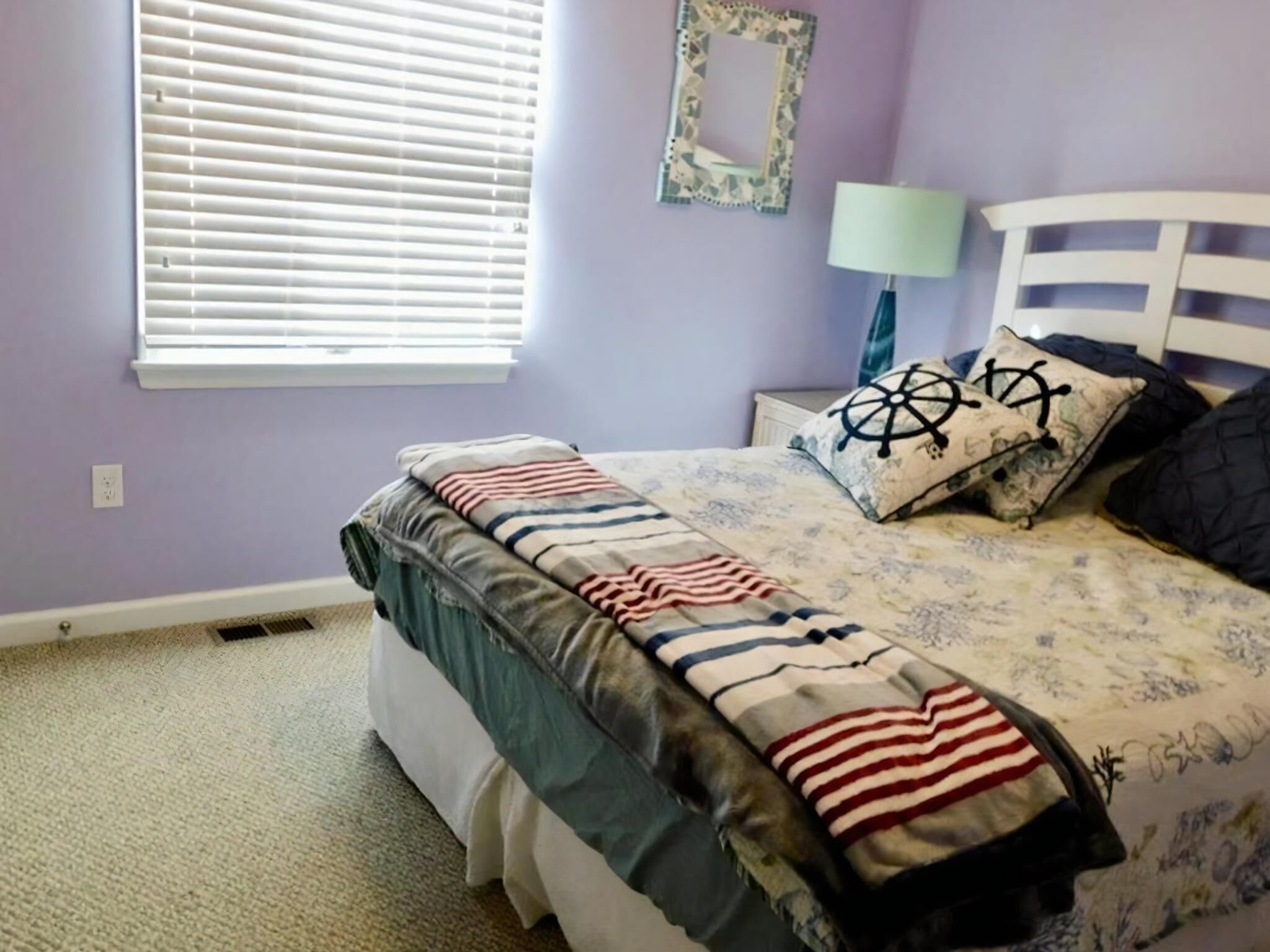 Un dormitorio con cama, ventana con persianas, mesita de noche y lámpara.