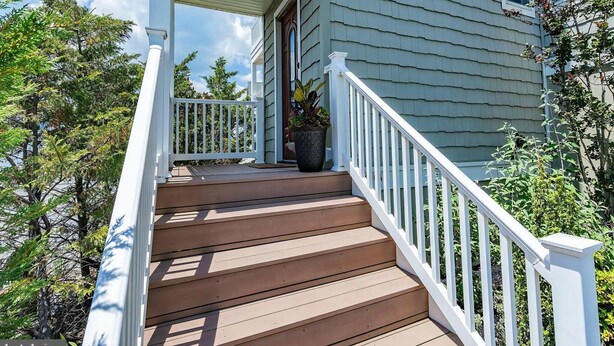 A wooden staircase leading to a porch with white railings, a potted plant, and a house with siding. - pet friendly vacation rental on LBI (Brant Beach)