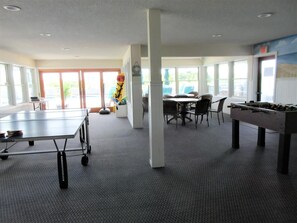 A room with a ping pong table, a foosball table, and a dining area with chairs and a table.