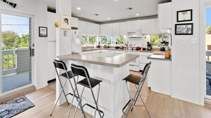 A modern kitchen with white cabinetry, a central island with bar stools, and a view of the outdoors. - 6 BEDROOMS ON PRIVATE LANE! (Loveladies)
