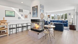 A modern living room with a fireplace, blue sofa, and a dining area. - 6 BEDROOMS ON PRIVATE LANE! (Loveladies)