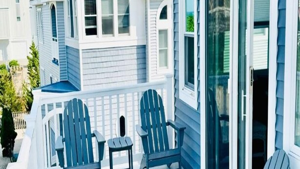 A covered porch with Adirondack chairs and a small table, overlooking a residential area.