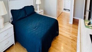 A bedroom with a large bed, bedside lamps, a window, and a door leading to another room.