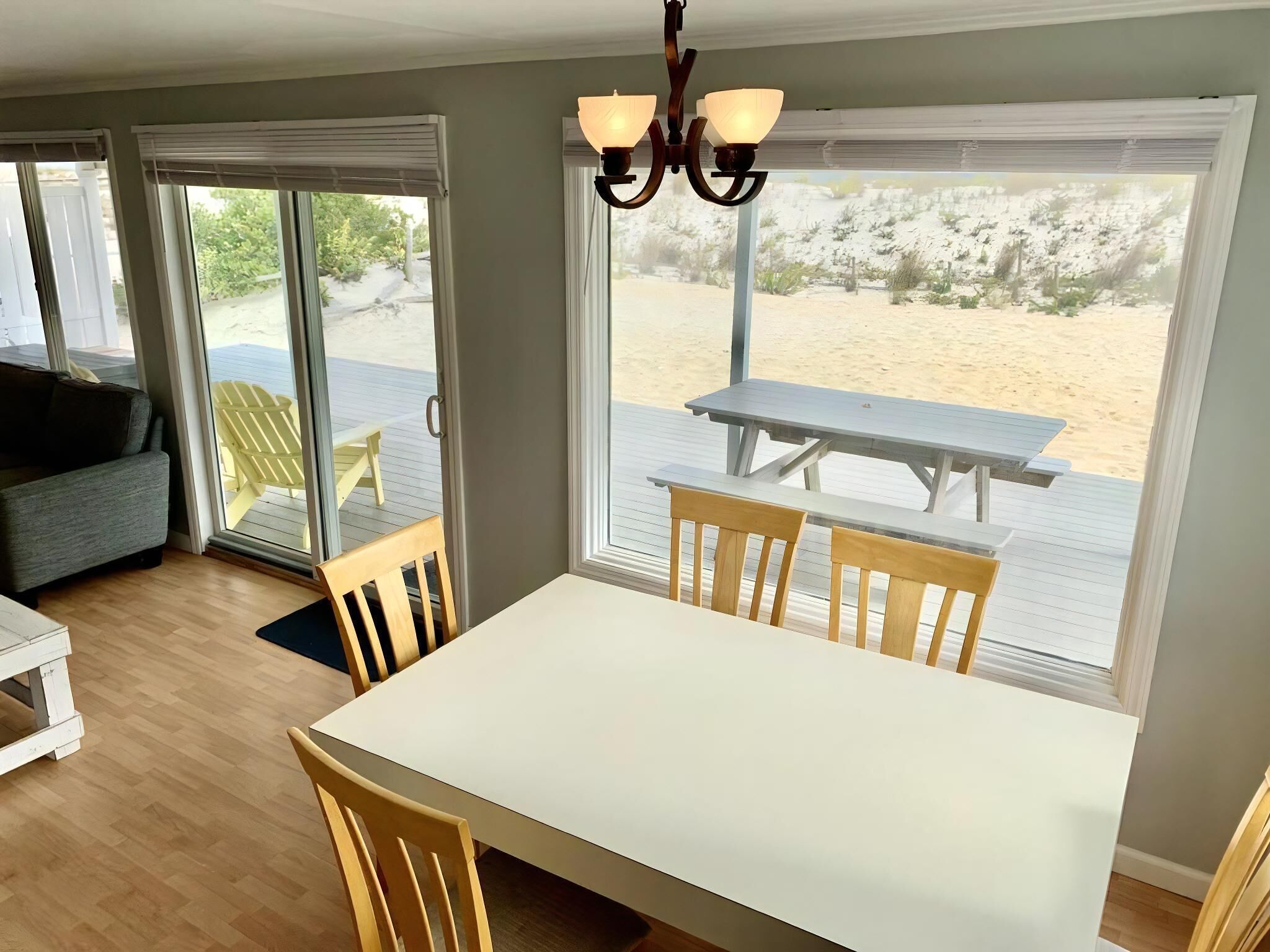 Un espace repas comprenant une table et des chaises, un lustre et de grandes fenêtres donnant sur une terrasse et une plage.